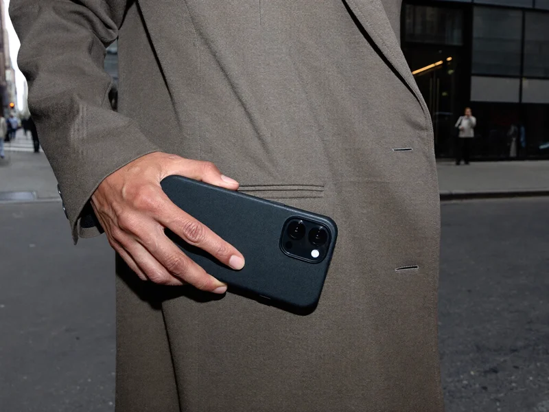 Hånd trækker telefon i beskyttende cover op af en frakkelomme på gaden